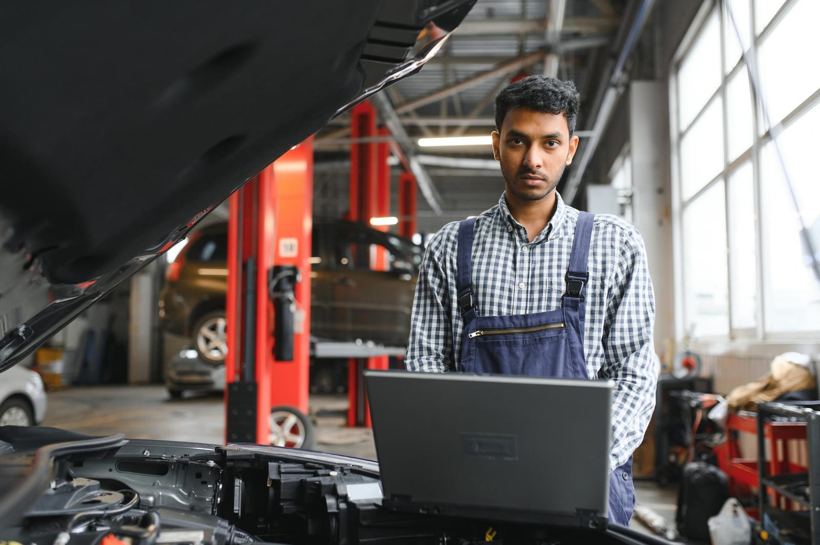 Mecânico com notebook ao lado de um carro em oficina, representando a seção de testes em vídeo
